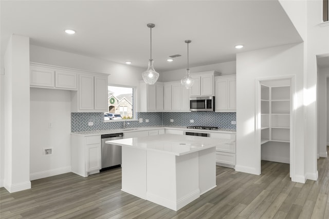 kitchen featuring light wood-type flooring, backsplash, stainless steel appliances, white cabinets, and a kitchen island