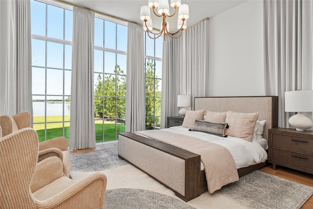 bedroom with a water view, access to outside, light hardwood / wood-style flooring, and a notable chandelier