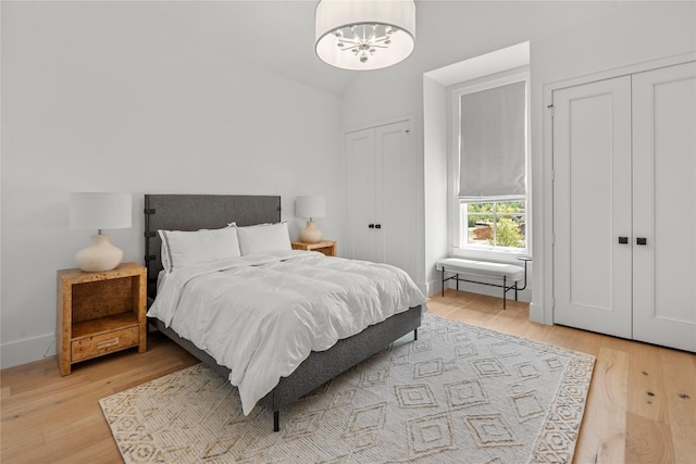 bedroom featuring a notable chandelier, vaulted ceiling, light hardwood / wood-style floors, and multiple closets