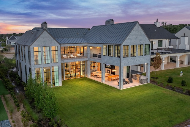 back house at dusk with an outdoor living space, a yard, a patio area, and a balcony