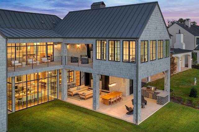 back house at dusk with exterior kitchen, a patio, an outdoor hangout area, and a yard