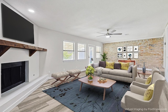 living room with hardwood / wood-style flooring, a textured ceiling, ceiling fan, and brick wall