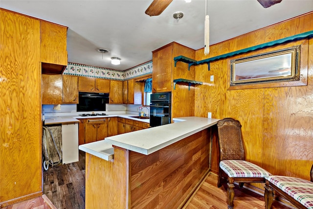 kitchen featuring kitchen peninsula, gas stovetop, sink, hardwood / wood-style flooring, and wood walls