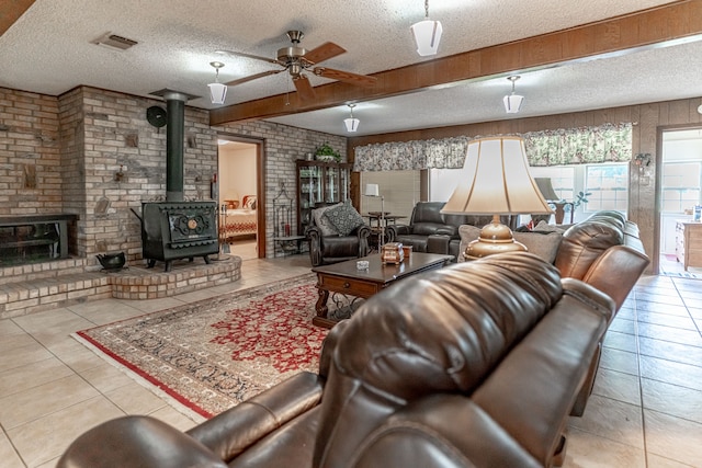 living room featuring a wood stove, light tile patterned floors, a textured ceiling, brick wall, and ceiling fan