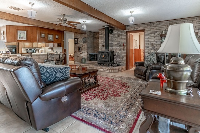 living room with beamed ceiling, a wood stove, a textured ceiling, and brick wall