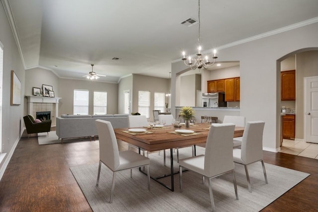 dining room with a tile fireplace, ceiling fan with notable chandelier, light hardwood / wood-style flooring, and ornamental molding