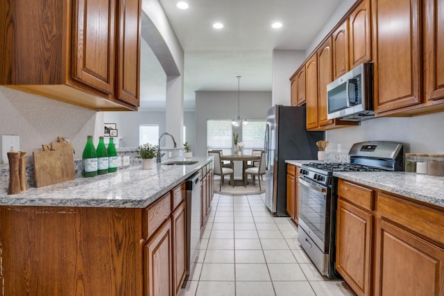 kitchen featuring pendant lighting, sink, light stone countertops, appliances with stainless steel finishes, and a notable chandelier