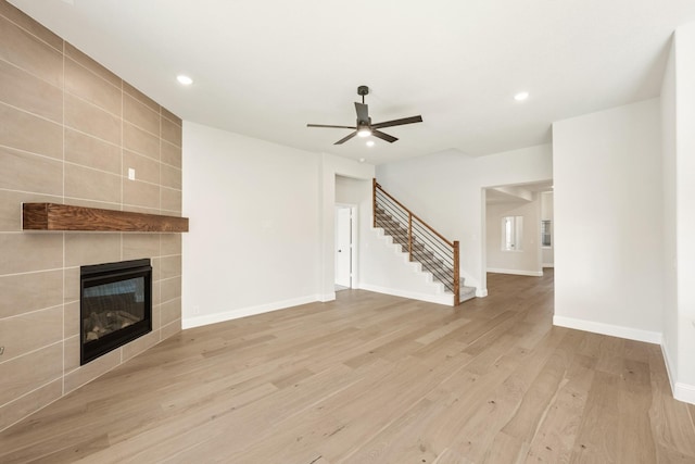 unfurnished living room with a tiled fireplace, ceiling fan, tile walls, and light wood-type flooring