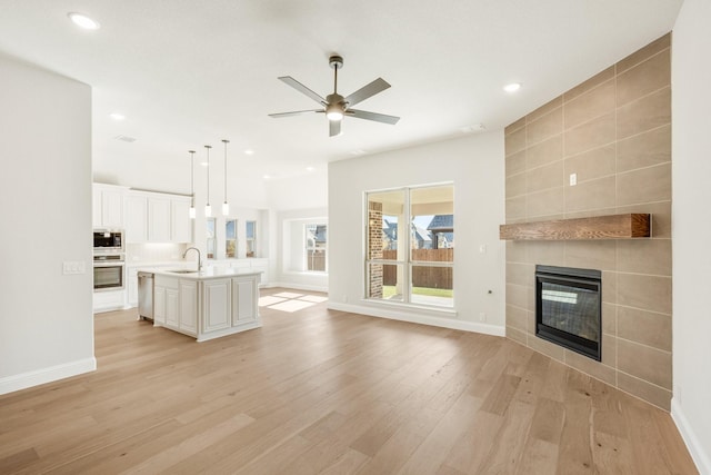 unfurnished living room with a tile fireplace, ceiling fan, sink, light hardwood / wood-style floors, and tile walls