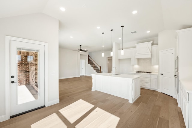 kitchen featuring custom range hood, pendant lighting, light hardwood / wood-style floors, lofted ceiling, and an island with sink