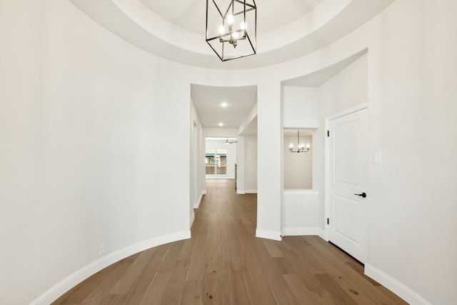 hall with a raised ceiling, a chandelier, and hardwood / wood-style flooring