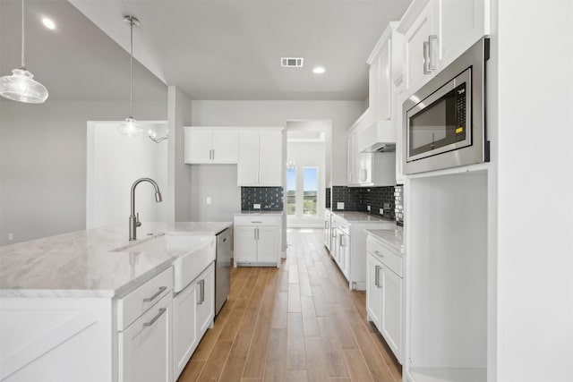 kitchen with appliances with stainless steel finishes, decorative light fixtures, sink, white cabinets, and a kitchen island with sink