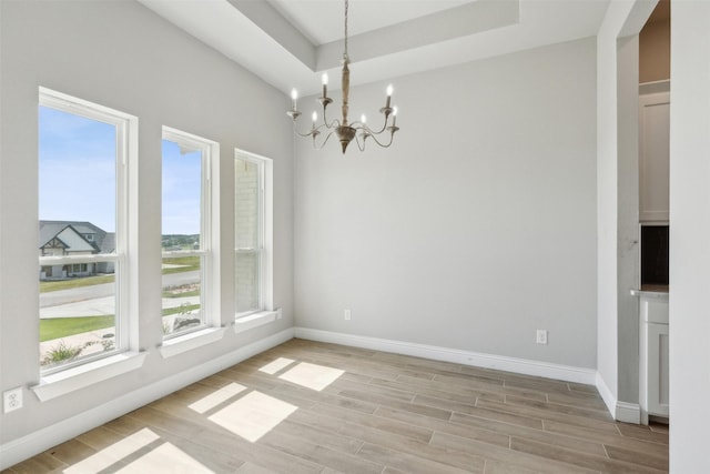 empty room featuring a notable chandelier, light wood-type flooring, and a tray ceiling