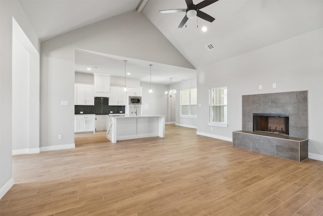 unfurnished living room featuring light hardwood / wood-style flooring, high vaulted ceiling, a tiled fireplace, ceiling fan with notable chandelier, and beamed ceiling