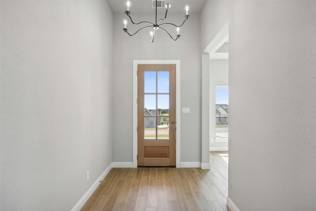 doorway with light wood-type flooring, a towering ceiling, and a chandelier