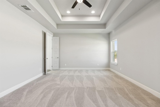 unfurnished room with a raised ceiling, light carpet, and ceiling fan