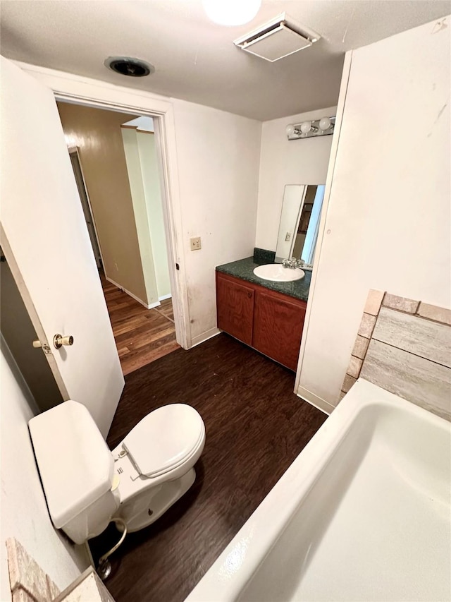 bathroom with vanity, a washtub, hardwood / wood-style flooring, and toilet