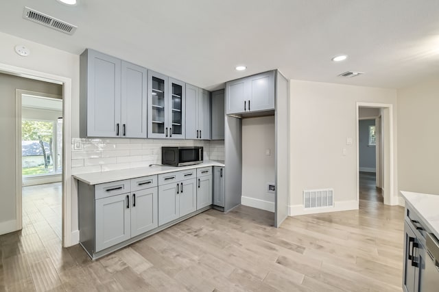 kitchen with gray cabinetry, light hardwood / wood-style floors, light stone countertops, and backsplash