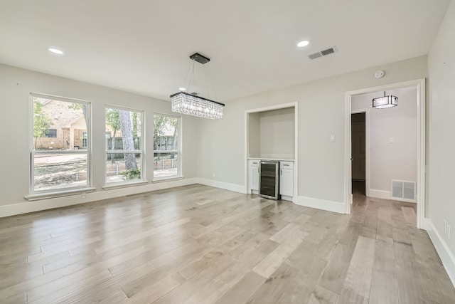 unfurnished living room featuring light hardwood / wood-style flooring, a chandelier, and beverage cooler