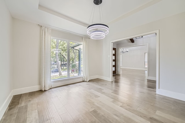 empty room featuring a raised ceiling, a notable chandelier, and light wood-type flooring