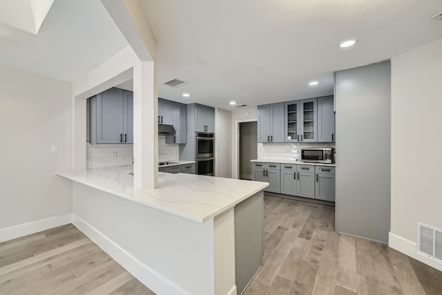 kitchen featuring stainless steel appliances, tasteful backsplash, light wood-type flooring, and gray cabinetry