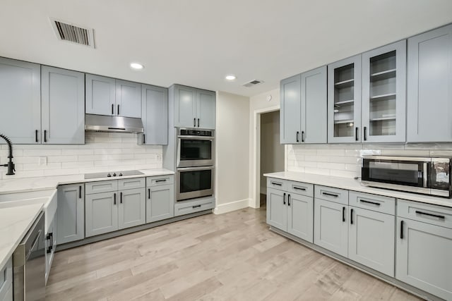 kitchen featuring light wood-type flooring, light stone countertops, backsplash, and stainless steel appliances