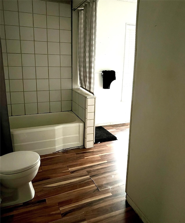 bathroom with hardwood / wood-style flooring, toilet, and tiled shower / bath