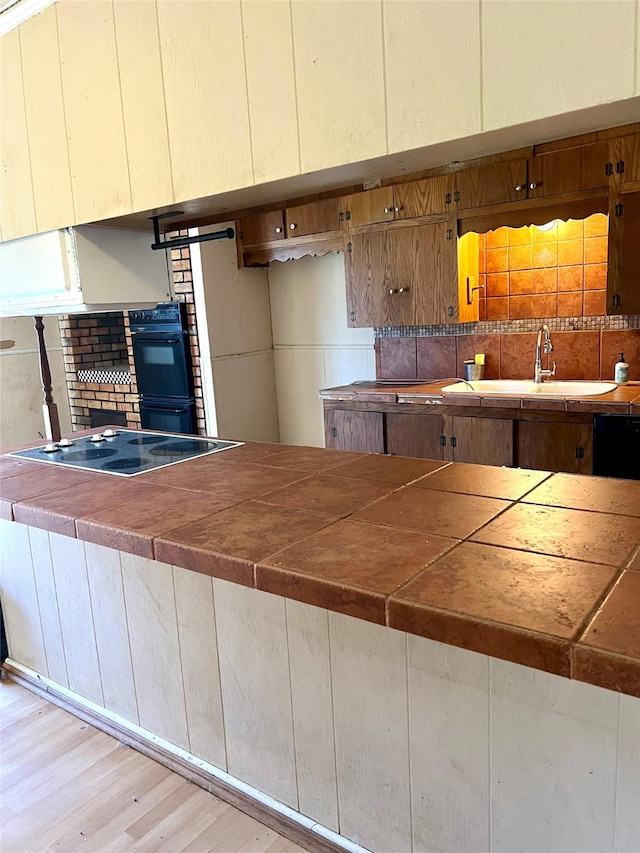 kitchen featuring sink, black double oven, light hardwood / wood-style flooring, and electric stovetop