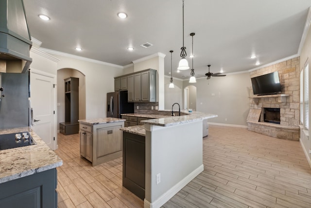 kitchen with a fireplace, ceiling fan, stainless steel refrigerator with ice dispenser, crown molding, and a kitchen island