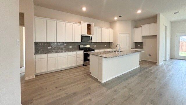 kitchen featuring a kitchen island with sink, appliances with stainless steel finishes, light wood-type flooring, and white cabinets