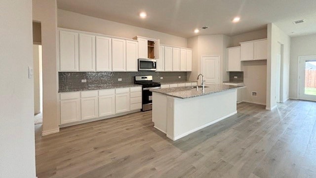 kitchen with light wood finished floors, an island with sink, stainless steel appliances, white cabinetry, and backsplash