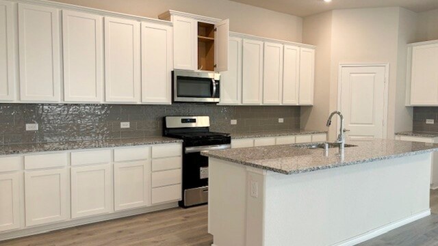 kitchen featuring white cabinets, light wood-type flooring, appliances with stainless steel finishes, sink, and a kitchen island with sink