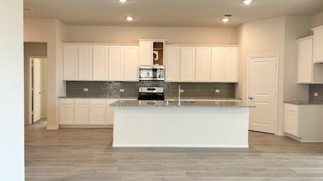 kitchen with white cabinets, light stone countertops, an island with sink, and range