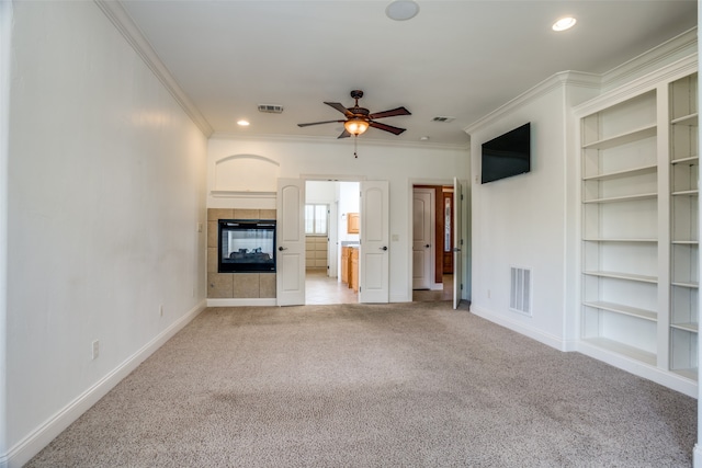 unfurnished living room featuring a fireplace, ceiling fan, built in shelves, ornamental molding, and carpet floors