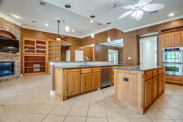 kitchen with ceiling fan, stainless steel appliances, pendant lighting, an island with sink, and a brick fireplace