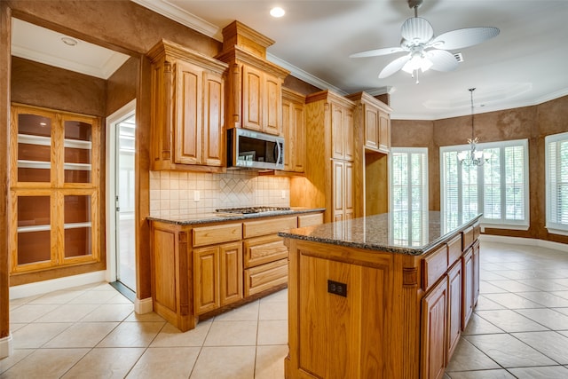 kitchen with stainless steel appliances, hanging light fixtures, a kitchen island, ceiling fan with notable chandelier, and light tile patterned flooring