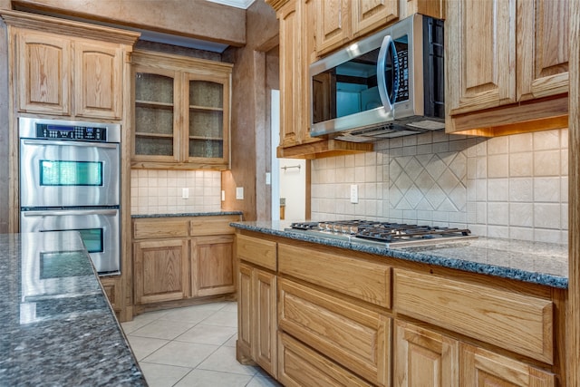 kitchen with appliances with stainless steel finishes, dark stone countertops, light tile patterned floors, and tasteful backsplash