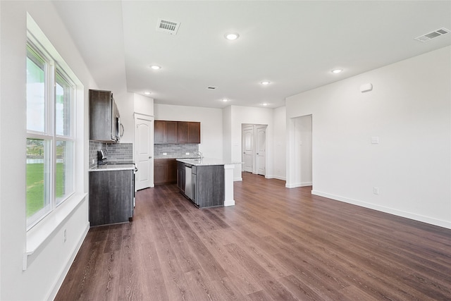 kitchen with dark wood-type flooring, backsplash, a healthy amount of sunlight, and a center island