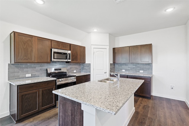 kitchen featuring light stone counters, an island with sink, dark hardwood / wood-style flooring, sink, and stainless steel appliances