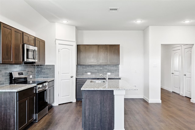 kitchen featuring dark hardwood / wood-style floors, an island with sink, stainless steel appliances, sink, and light stone countertops