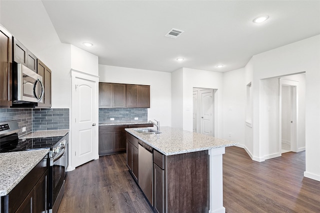 kitchen with dark hardwood / wood-style floors, a center island with sink, sink, light stone countertops, and appliances with stainless steel finishes