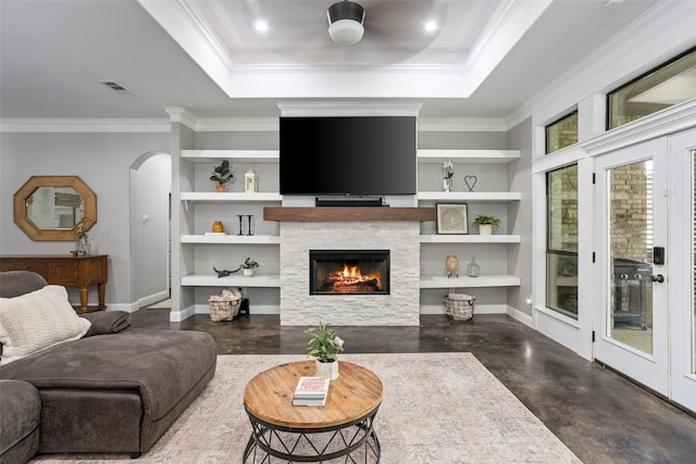 living room with built in shelves, ornamental molding, a tray ceiling, and a fireplace