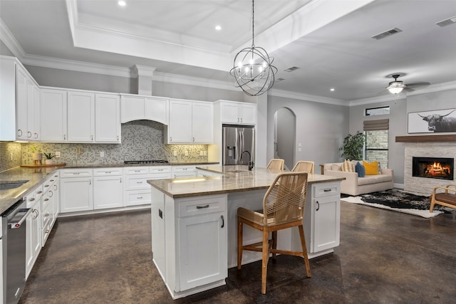 kitchen featuring a center island with sink, stainless steel appliances, a fireplace, white cabinetry, and decorative light fixtures