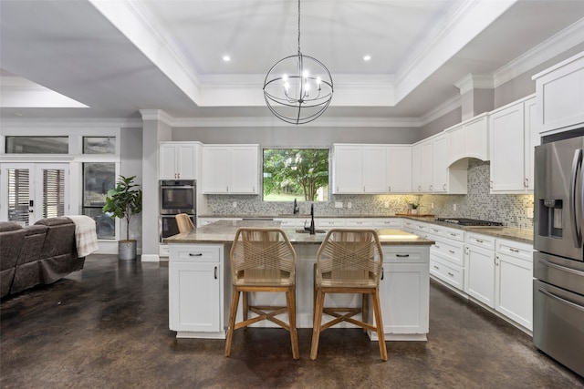 kitchen with a center island with sink, a raised ceiling, hanging light fixtures, and appliances with stainless steel finishes