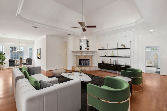 living room featuring a premium fireplace, ceiling fan with notable chandelier, a raised ceiling, and light hardwood / wood-style flooring