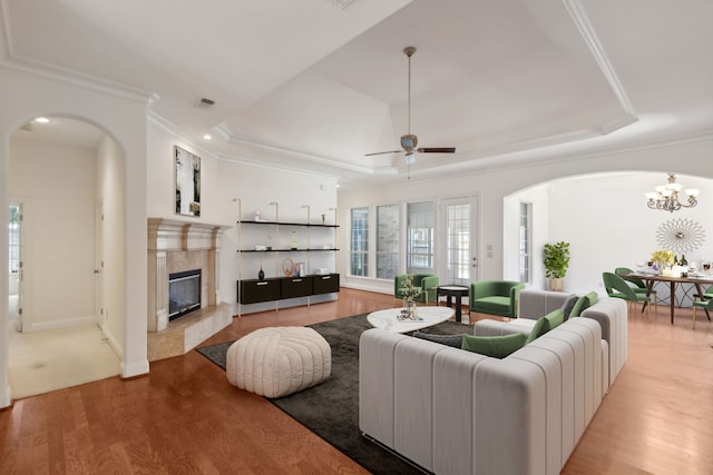 living room featuring ceiling fan with notable chandelier, a fireplace, ornamental molding, a tray ceiling, and light wood-type flooring