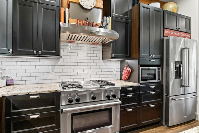 kitchen featuring tasteful backsplash, light stone counters, exhaust hood, light hardwood / wood-style flooring, and high quality appliances