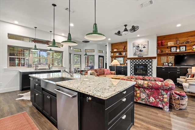 kitchen featuring dishwasher, a tile fireplace, sink, built in shelves, and an island with sink