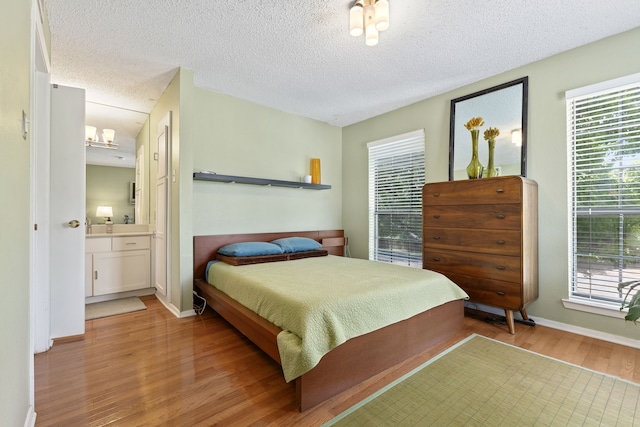 bedroom featuring multiple windows, ensuite bathroom, a textured ceiling, and light hardwood / wood-style flooring