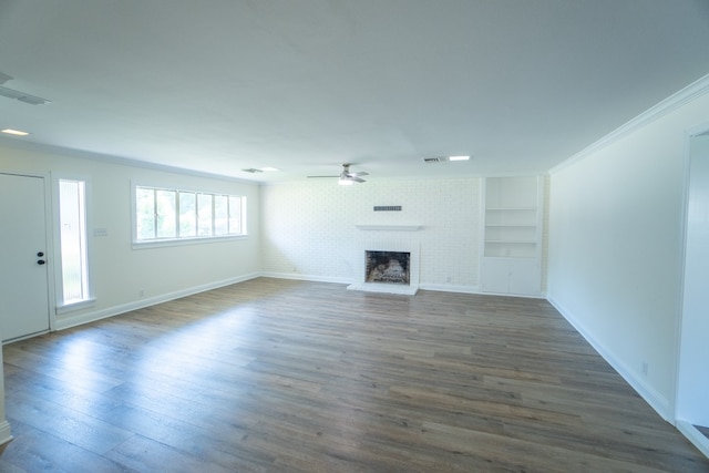 unfurnished living room with ceiling fan, dark wood-type flooring, built in features, crown molding, and a fireplace